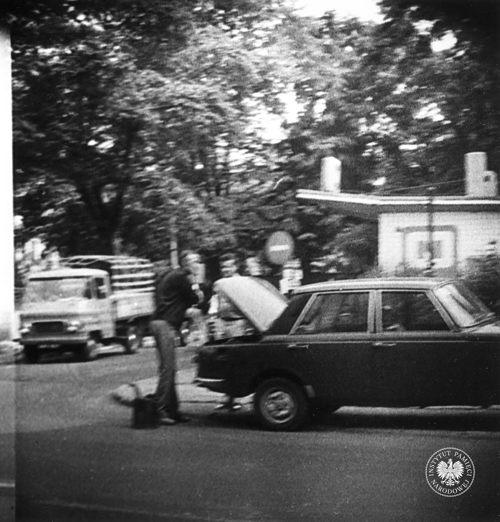 Przykładowa fotografia operacyjna, wykonana z ukrycia podczas obserwacji. Dwaj mężczyźni stoją przy samochodzie marki Wartburg obok stacji CPN. Zdjęcie jest poruszone, zrobiono je w sierpniu 1982 r. (IPN Ka 435/9)